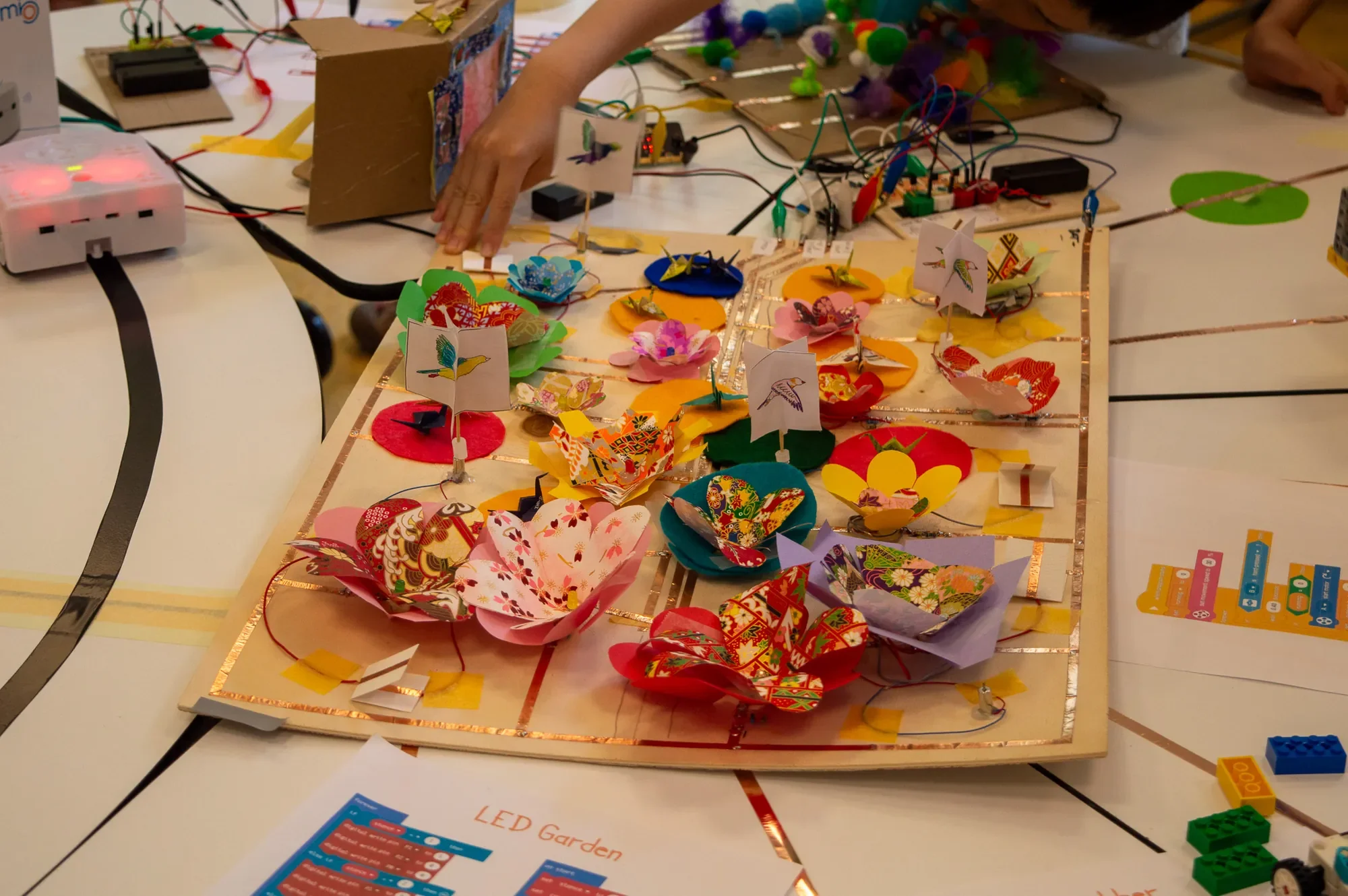 Kinderhand an einer Papierblumenwiese mit LEDs, Kupferklebeband und Schaltern
