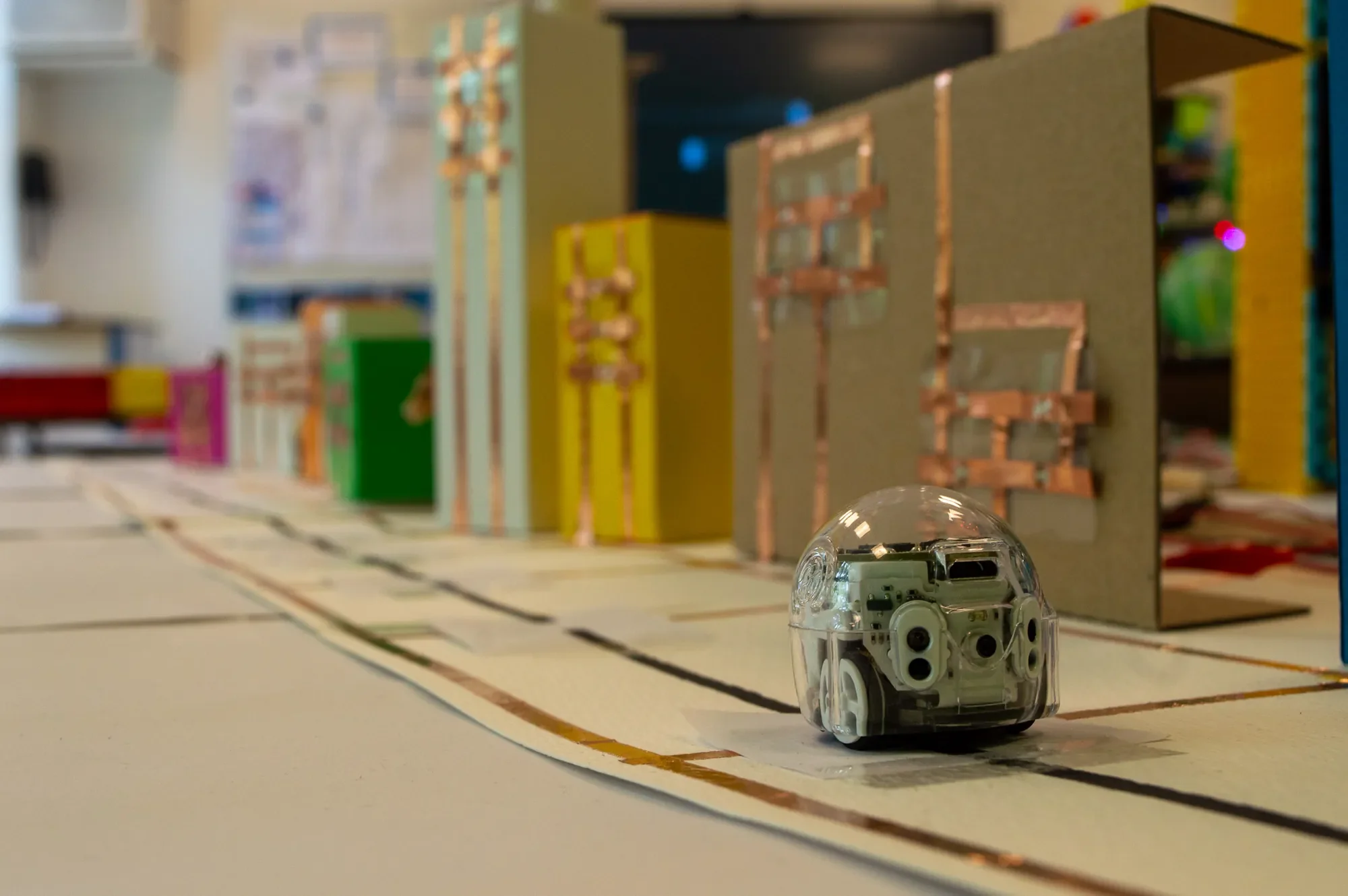 Ozobot-Roboter auf einer Straße aus Kreppband zwischen Häusern mit Kupferband-Schaltkreisen