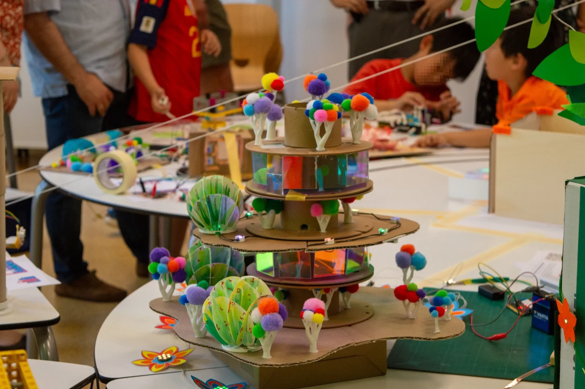 Mehrstöckiger Kartonturm mit Papierbäumen, Pompons und holografischen Fenstern